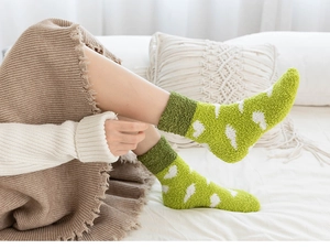 Gros plan de chaussettes douillettes en polaire verte avec motifs de cœur sur lit blanc