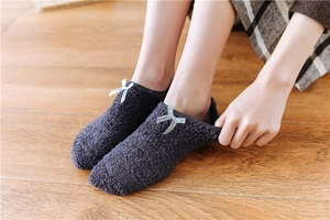 Close-up of dark grey plush floor socks with silver-blue bow detail on wooden background