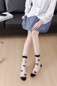 Close-up of white mesh socks with black bow patterns and scalloped elastic cuffs