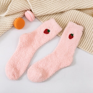 Detail of pink coral fleece socks with strawberry embroidery on cozy knit background