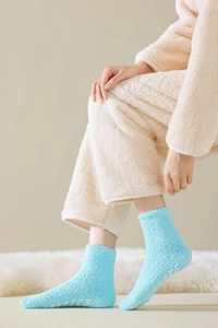Detail of light blue fuzzy socks with white anti-slip dots on a soft carpet