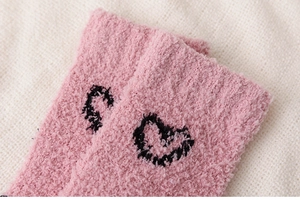 Gros plan de chaussettes en molleton corail rose avec motif de cœur noir et peluche