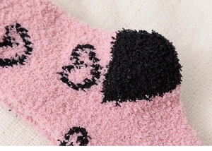 Gros plan de chaussettes en polaire corail rose doux avec motif cœur noir et peluche
