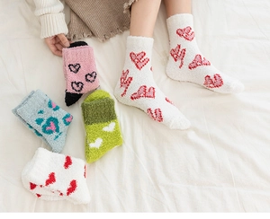 Gros plan de chaussettes douces en polaire corail à motifs cœurs sur un drap blanc