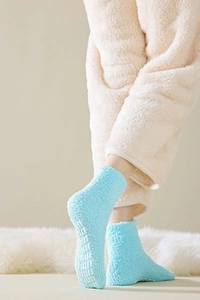 Detail of blue fuzzy thermal socks with white anti-slip dots on a soft plush rug