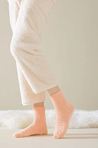 Detail of light orange fuzzy socks with anti-slip dots on a soft white carpet background