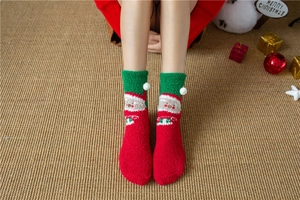 Detail of red and green coral fleece socks featuring Santa Claus patterns and fuzzy pom-poms