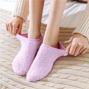 Close-up of soft pink coral fleece slipper socks on beige knit blanket for winter warmth