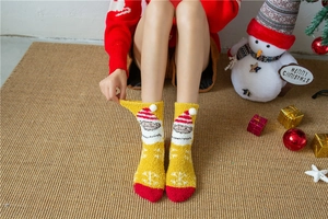 Detail of yellow coral fleece Christmas socks featuring 3D plush balls and Santa patterns