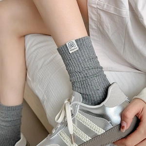 Close-up of grey ribbed knit mid-tube socks with white woven label and silver athletic shoes
