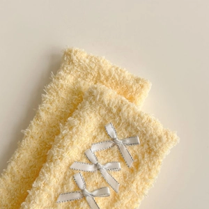 Detail of yellow coral fleece socks featuring elegant white satin bows with silver trim