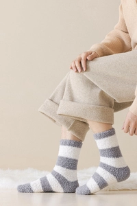 Detail of soft coral fleece striped home socks worn on a white plush carpet