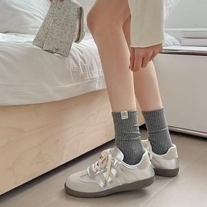 Detail of dark gray ribbed crew socks with a small fabric tag and retro style sneakers
