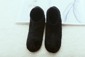 Close-up of black fleece indoor slipper socks laid on a soft plush white carpet