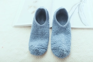 Close-up of light blue plush slipper socks with soft fleece texture on a white rug