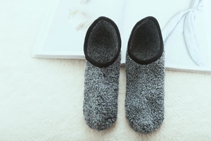 Detail of plush grey indoor slipper socks with warm fleece lining on a white rug