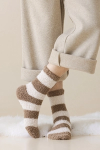 Detail of warm brown and white striped coral fleece socks worn on a plush white carpet