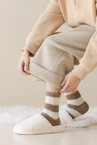 Detail of striped coral fleece warm socks with plush indoor slippers in a cozy home setting
