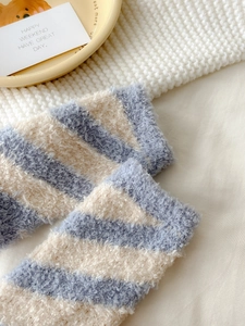 Close-up of blue and off-white striped coral fleece socks on a cozy knitted blanket