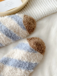 Close-up of soft blue and brown striped coral fleece socks on a cozy knit blanket