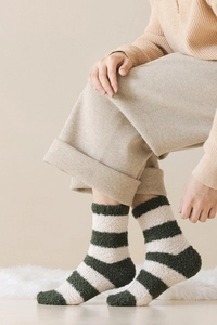 Close-up of green and beige striped coral fleece socks worn on a cozy white rug