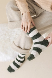 Detailed close-up of green and white striped coral fleece socks worn in a cozy home setting