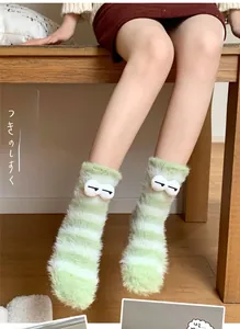 Close-up of fluffy green and white striped coral fleece socks with cute cartoon eyes