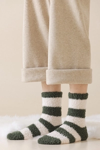 Close-up of green and white striped coral fleece socks worn in a cozy home setting