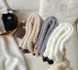Detailed view of plush coral fleece winter socks with cute 3D pom-pom and cartoon eye embroidery