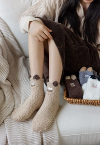 Close-up of fluffy coral fleece socks with cute cartoon 3D ears on a cozy home sofa