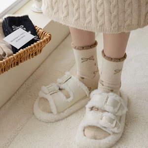 Close-up of fluffy cream slippers with buckles and bow pattern thermal socks on a rug