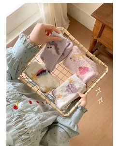 Close-up of fluffy coral fleece socks with unicorn embroidery in a white wire basket