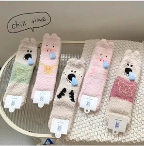 Five pairs of fluffy coral fleece socks with 3D cartoon animal charms on a white knit rug
