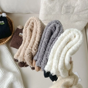 Three pairs of thick fuzzy coral fleece socks with cute cartoon eyes in a cozy home setting