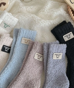 Close-up of fluffy coral fleece socks with cute bear patch labels in pastel colors