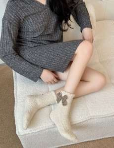 Detail of coral fleece socks with brown plaid bows on textured white sofa background