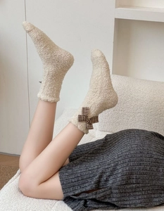 Detail of coral fleece mid-calf sock with a brown plaid bow in a cozy home setting