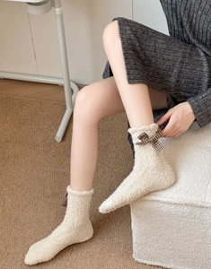 Detail of coral fleece socks with brown plaid bow and ruffled cuffs on carpet