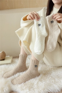 Dettaglio di calze in pile di corallo con ricamo a occhio nei colori crema e kaki