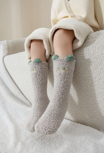 Détail de chaussettes en peluche grises avec oreilles 3D vertes et broderie mignonne
