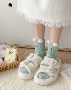 Detail of coral fleece socks with pom-poms and plush platform slippers on home rug