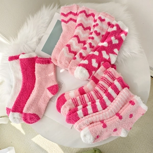 Detail view of pink coral fleece socks featuring heart and stripe patterns on plush mat