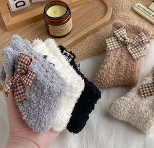 Close-up of soft coral fleece socks with plaid bows and elegant lifestyle props