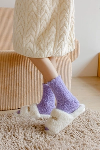 Dettaglio di calze in pile corallo e pantofole in peluche bianco con ricamo dorato