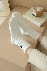 Dettaglio di calze in pile corallo bianco con ricamo minimalista a occhio per calore invernale