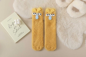 Detail of yellow fuzzy socks with funny 3D eyes and blue tongue on cozy white fur rug