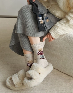Detail of cream cable-knit bear socks paired with white fluffy slippers in a cozy setting
