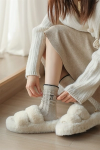 Detail of beige cable-knit wool socks featuring delicate black bow embroidery