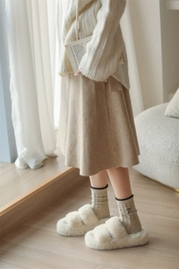 Detail of khaki cable knit wool socks paired with white faux fur slippers on wood floor