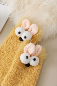 Close-up of yellow coral fleece socks with cute 3D cartoon eyes on soft plush blanket